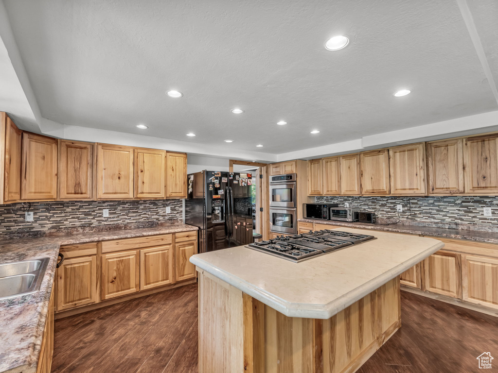 Kitchen with appliances with stainless steel finishes, dark wood-style floors, backsplash, recessed lighting, and a kitchen island
