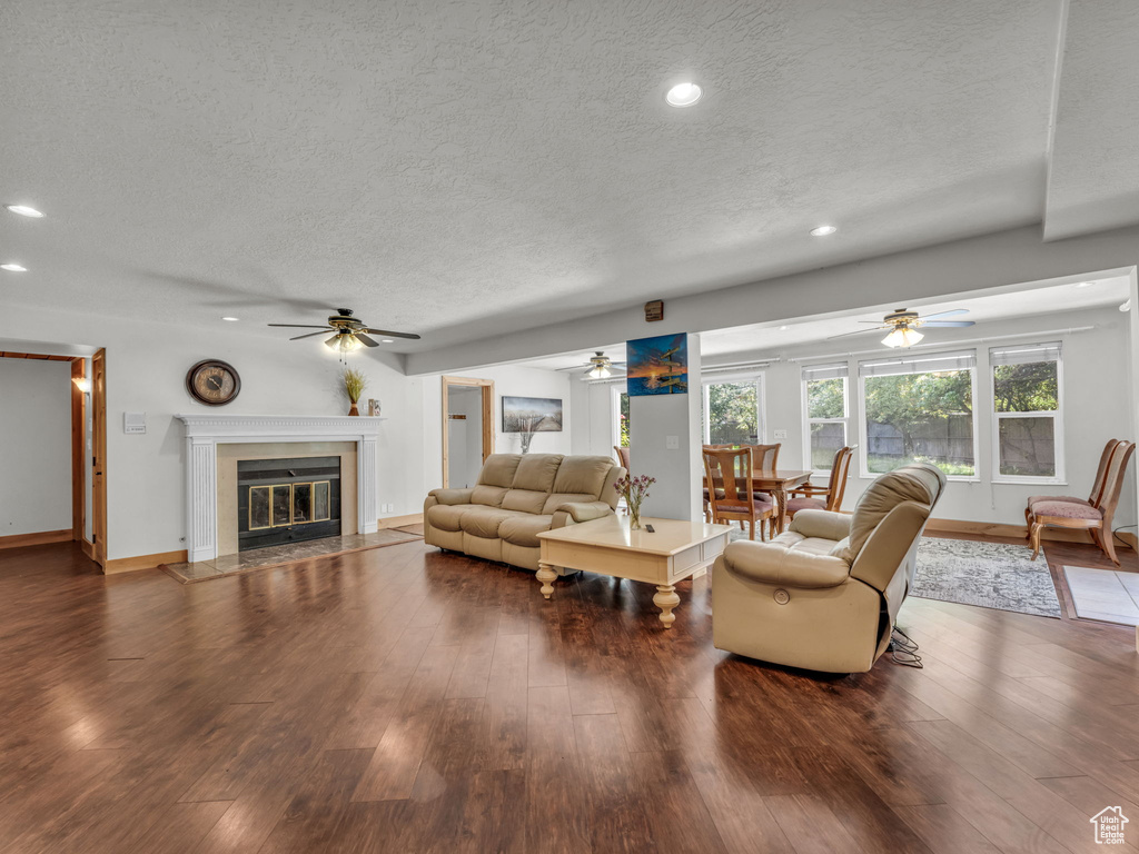 Living area featuring a textured ceiling, a ceiling fan, a tiled fireplace, wood finished floors, and recessed lighting