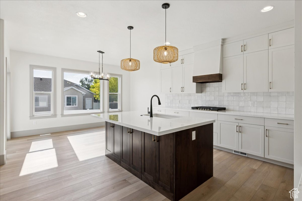 Kitchen featuring custom exhaust hood, light wood-type flooring, light countertops, stainless steel gas stovetop, and decorative backsplash
