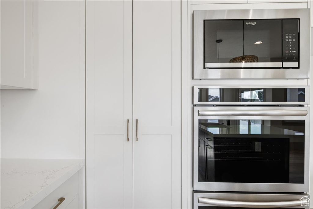Kitchen view of oven, built in microwave, white cabinetry, and light stone countertops