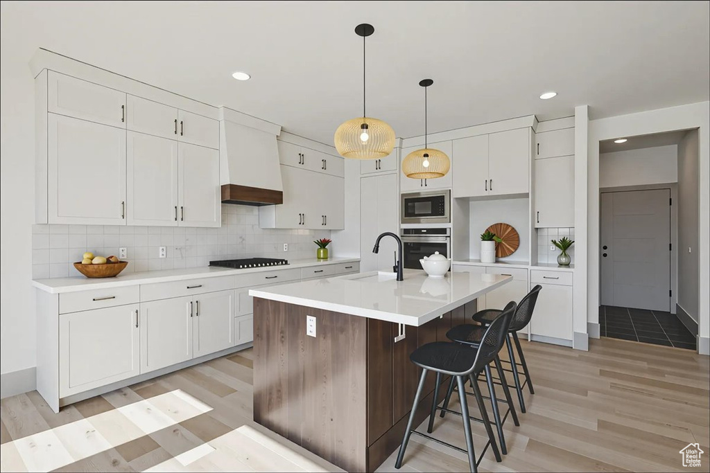 Kitchen featuring appliances with stainless steel finishes, light wood-style floors, white cabinets, tasteful backsplash, and light countertops