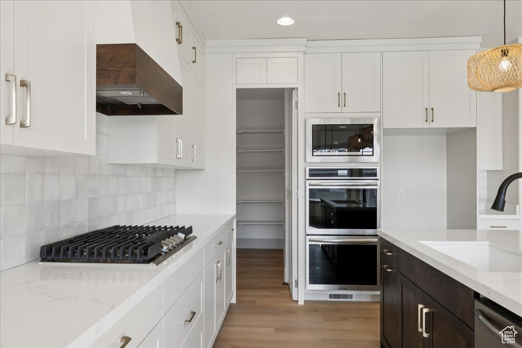 Kitchen with appliances with stainless steel finishes, white cabinets, light wood-style floors, custom exhaust hood, and recessed lighting