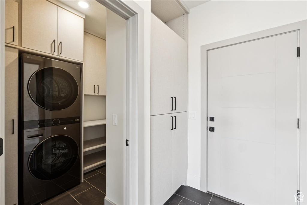 Laundry room with stacked washer / drying machine, cabinet space, and dark tile patterned flooring
