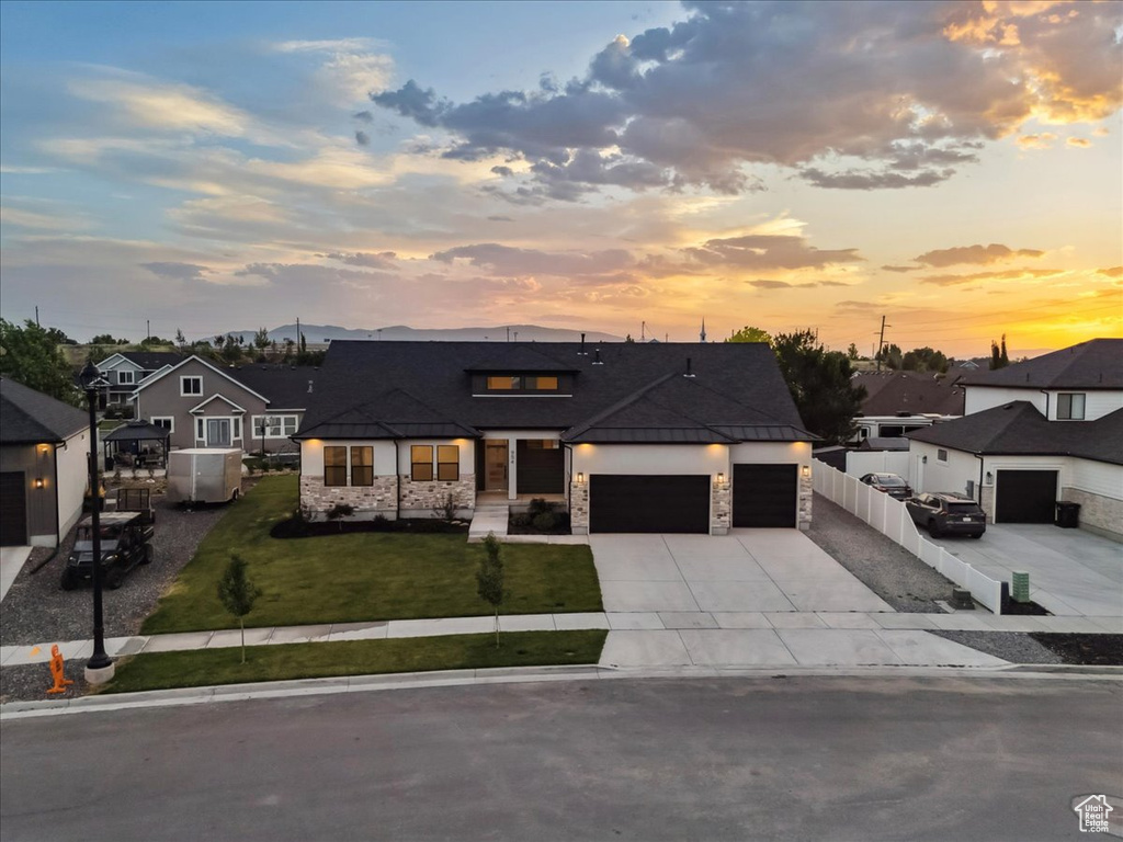 View of front of house with stone siding, a garage, concrete driveway, a lawn, and a residential view