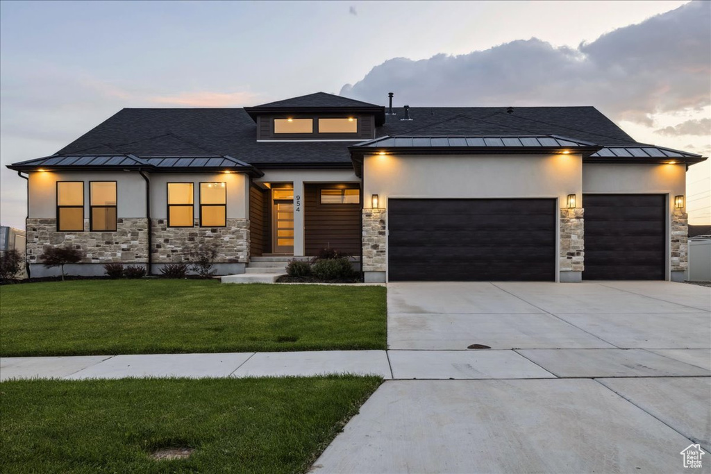 View of front of house featuring a standing seam roof, stone siding, a garage, a lawn, and concrete driveway