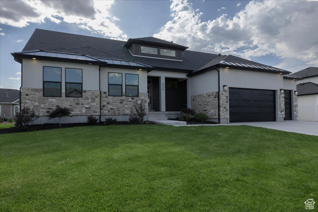 Prairie-style home featuring a garage, stone siding, driveway, and a front lawn