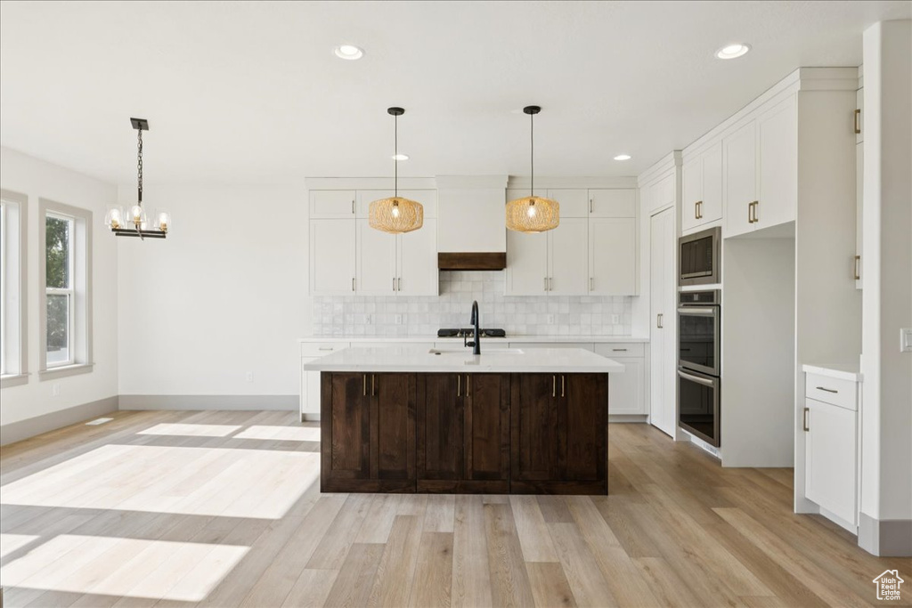 Kitchen with appliances with stainless steel finishes, light countertops, tasteful backsplash, a chandelier, and light wood-type flooring