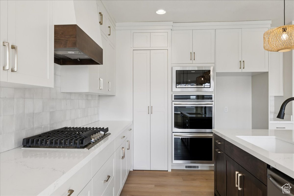 Kitchen with stainless steel appliances, white cabinetry, custom range hood, light stone counters, and recessed lighting