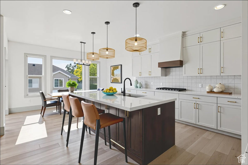 Kitchen featuring stovetop, light wood finished floors, tasteful backsplash, light countertops, and a center island with sink