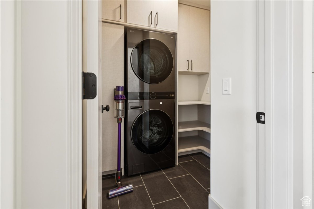 Laundry area with estacked washer and dryer, cabinet space, and dark tile patterned floors