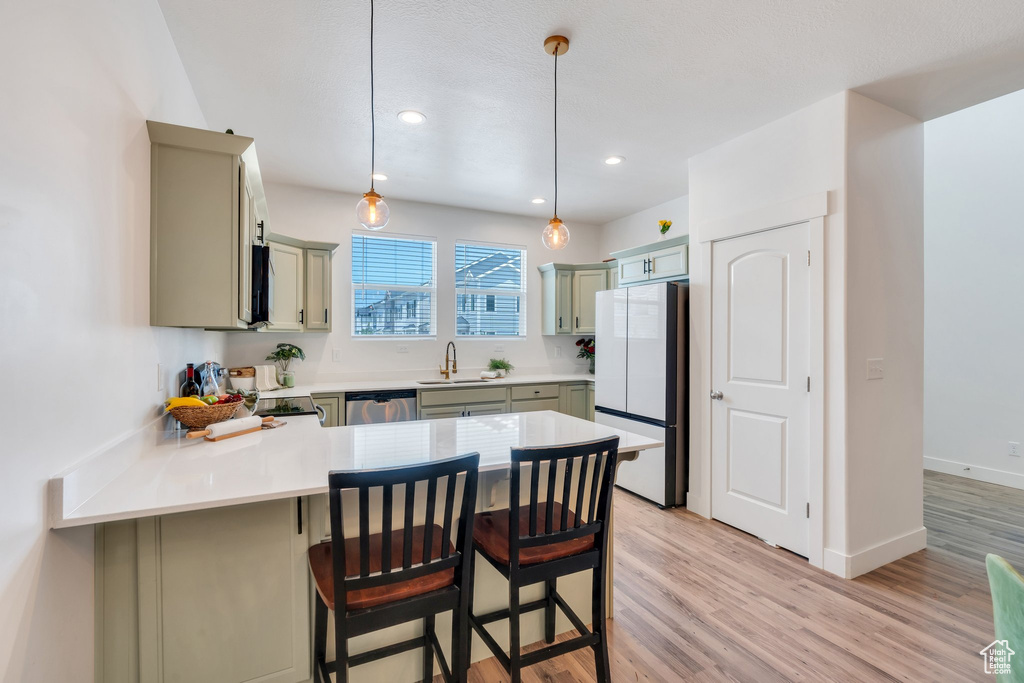 Kitchen with appliances with stainless steel finishes, a peninsula, light countertops, light wood-style floors, and a kitchen breakfast bar