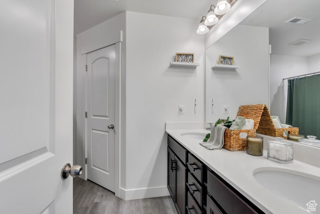 Full bath with wood finished floors, double vanity, and curtained shower
