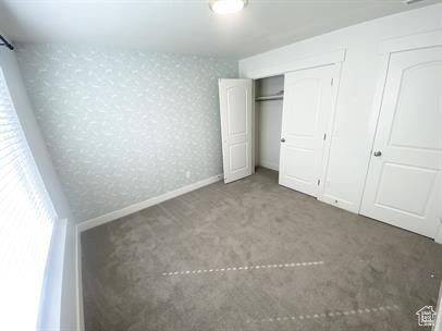 Unfurnished bedroom featuring carpet flooring, wallpapered walls, and a closet