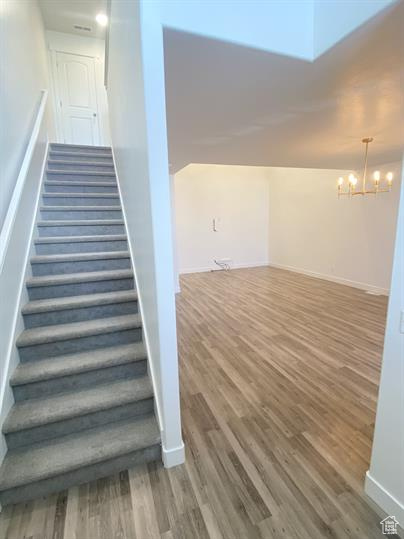 Staircase with wood finished floors and a chandelier