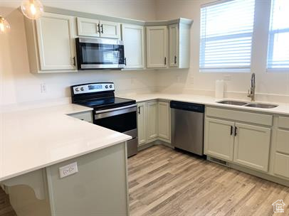 Kitchen featuring stainless steel appliances, a peninsula, light countertops, light wood-style floors, and pendant lighting