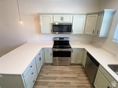Kitchen featuring stainless steel appliances, a peninsula, light countertops, light wood-style flooring, and pendant lighting