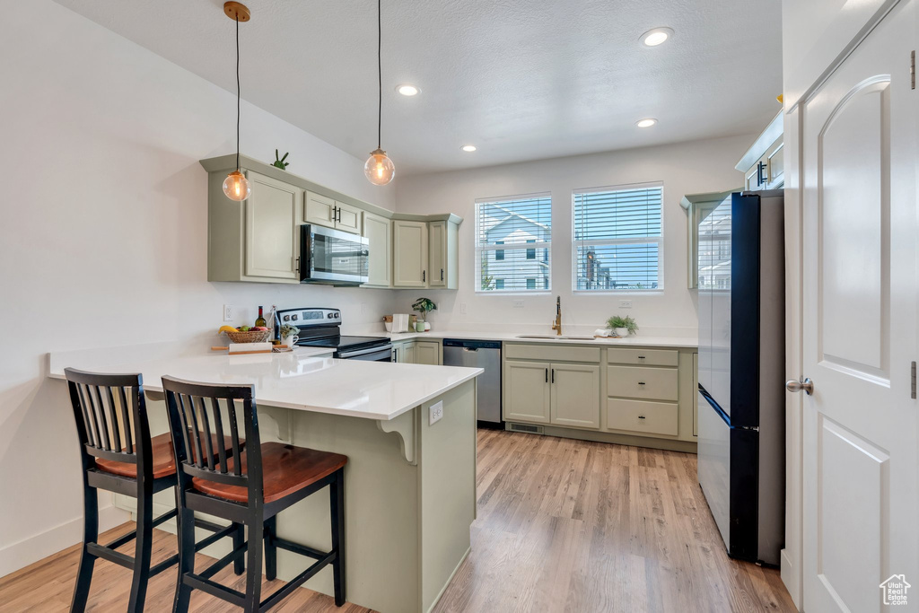 Kitchen with appliances with stainless steel finishes, a peninsula, a kitchen bar, light wood-type flooring, and pendant lighting