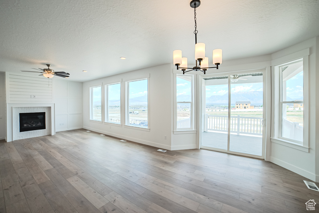 Unfurnished living room with a textured ceiling, ceiling fan, a chandelier, hardwood / wood-style floors, and a fireplace