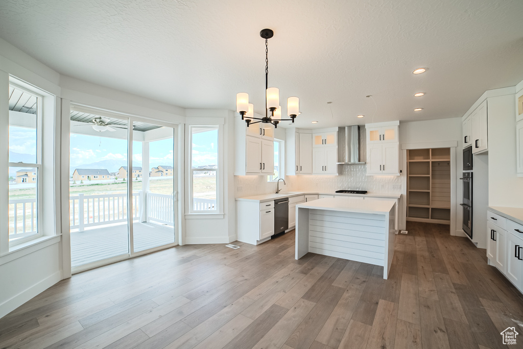 Kitchen featuring dishwasher, wall chimney range hood, a chandelier, stovetop, and a center island