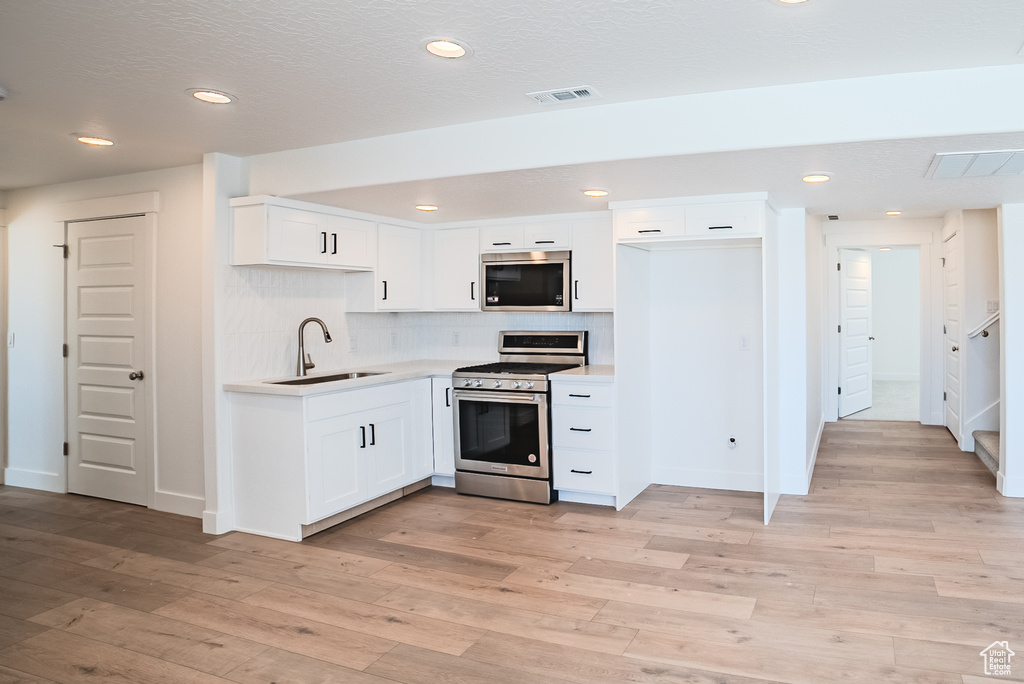 Kitchen featuring appliances with stainless steel finishes, light countertops, backsplash, light wood-style flooring, and white cabinets