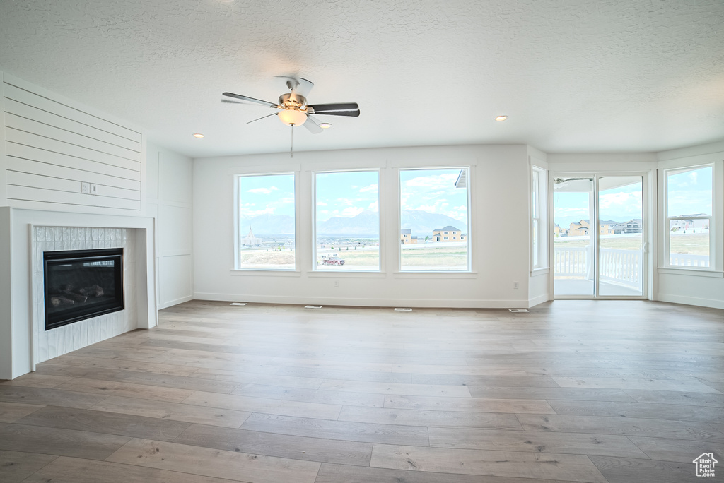 Unfurnished living room featuring ceiling fan, a tiled fireplace, hardwood / wood-style floors, recessed lighting, and a textured ceiling
