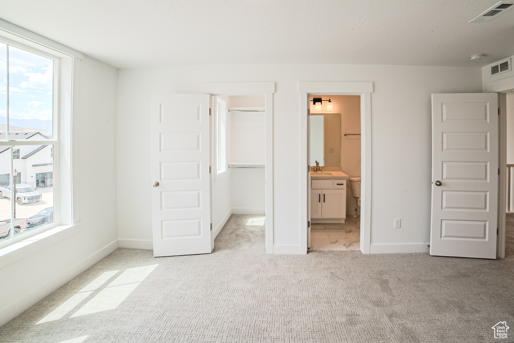 Unfurnished bedroom with light carpet, a walk in closet, multiple windows, and a closet