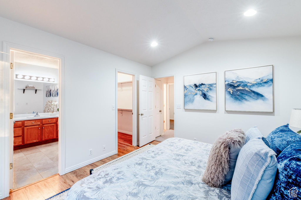Bedroom with light wood-style flooring, lofted ceiling, a spacious closet, connected bathroom, and recessed lighting