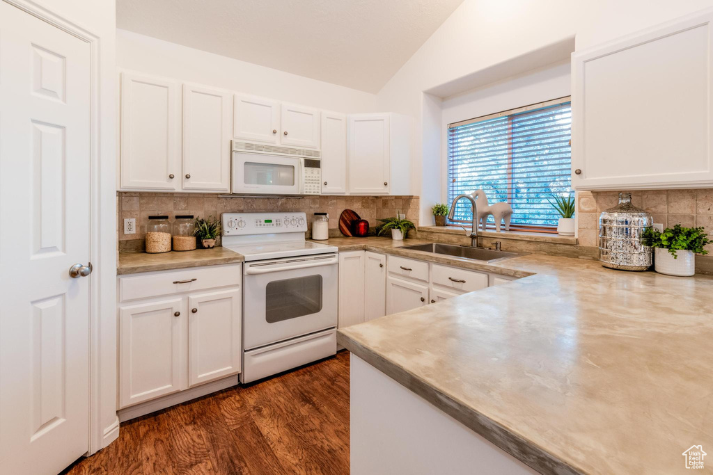 Kitchen featuring white appliances, lofted ceiling, white cabinets, and backsplash