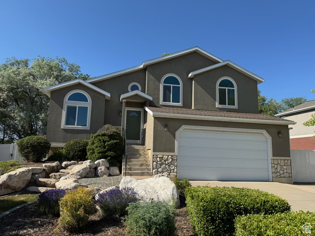 View of front of house with stucco siding, concrete driveway, an attached garage, and stone siding