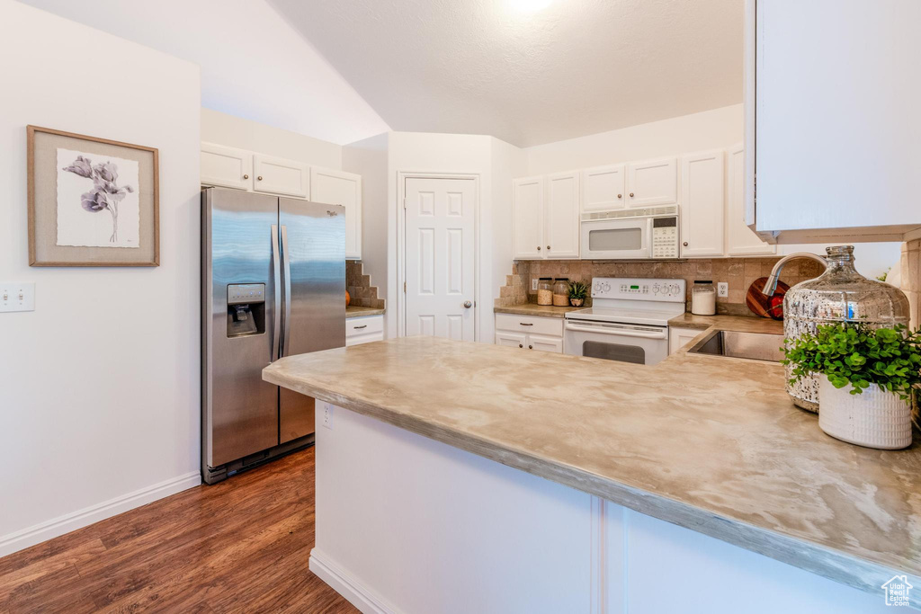 Kitchen with white appliances, a peninsula, white cabinets, and dark wood-style floors
