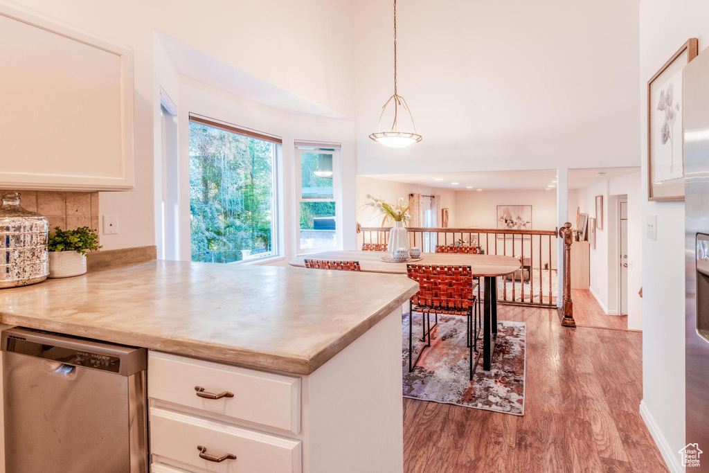 Kitchen featuring dishwasher, wood finished floors, white cabinetry, light countertops, and a towering ceiling