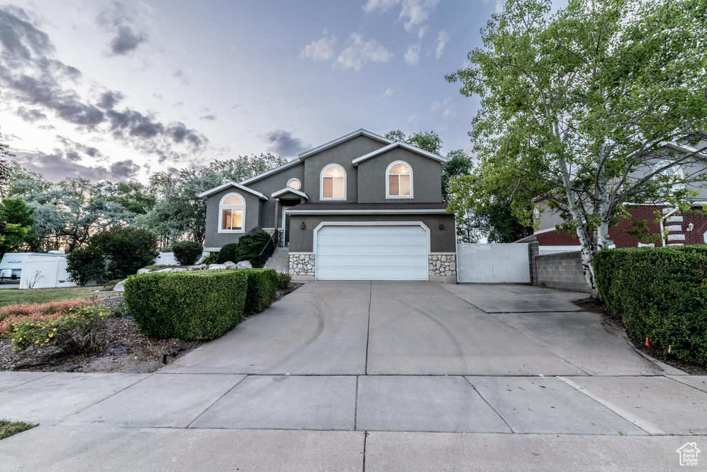 View of front of house with driveway, stucco siding, a garage, a gate, and stone siding