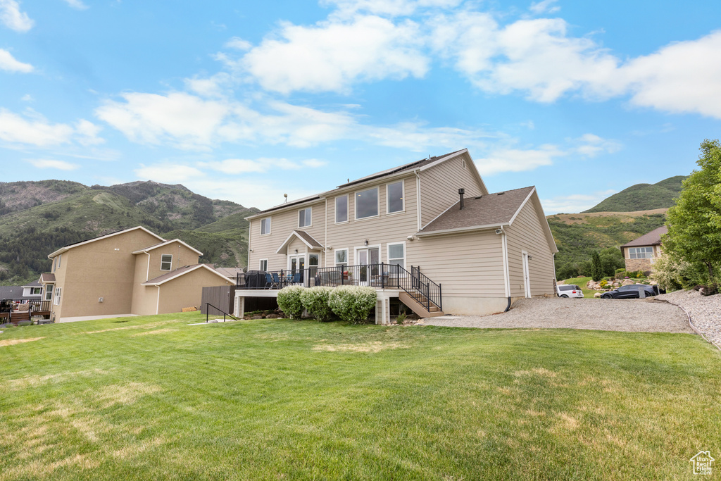 Back of property featuring stairs, a deck with mountain view, and a lawn