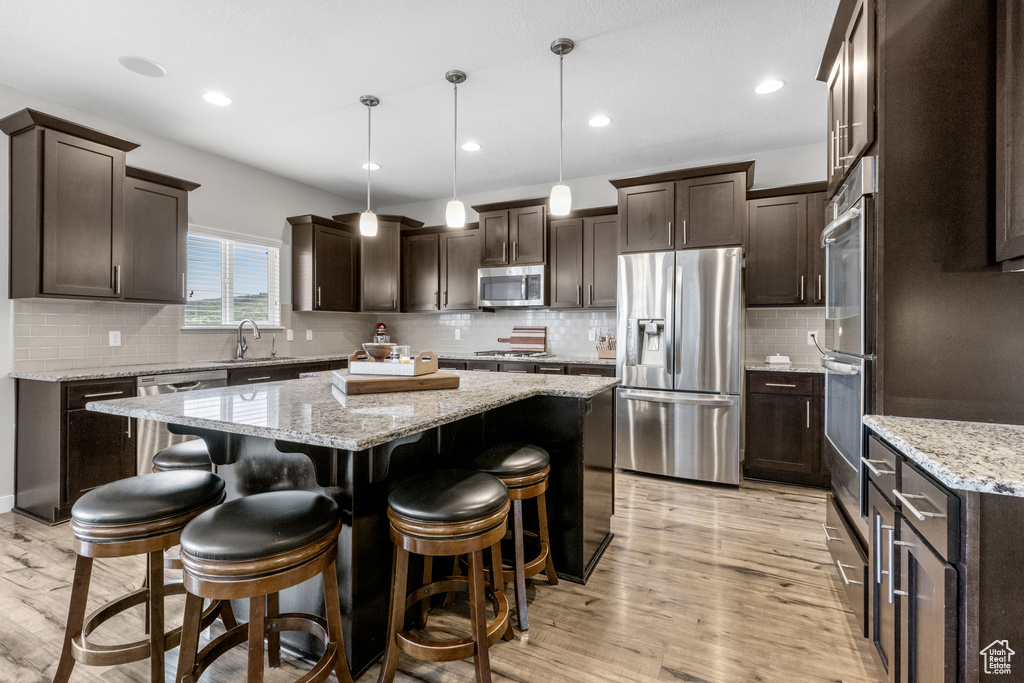 Kitchen featuring stainless steel appliances, dark brown cabinets, a center island, light wood-style floors, and recessed lighting
