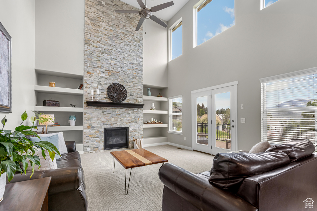 Carpeted living room featuring a high ceiling, ceiling fan, built in features, and a stone fireplace