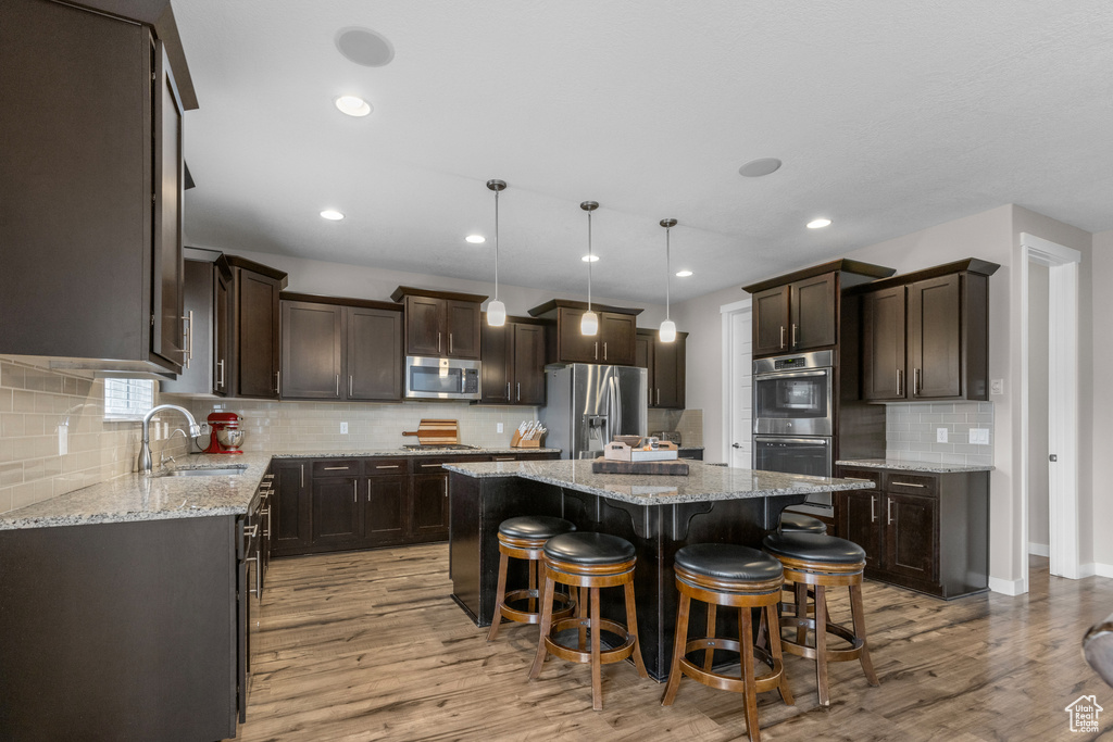 Kitchen with stainless steel appliances, dark brown cabinets, a center island, decorative backsplash, and a breakfast bar area