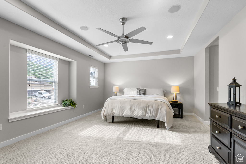 Bedroom with a tray ceiling, light carpet, ceiling fan, and recessed lighting