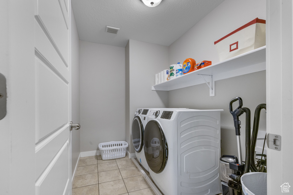 Laundry area with washing machine and clothes dryer, a textured ceiling, and light tile patterned flooring