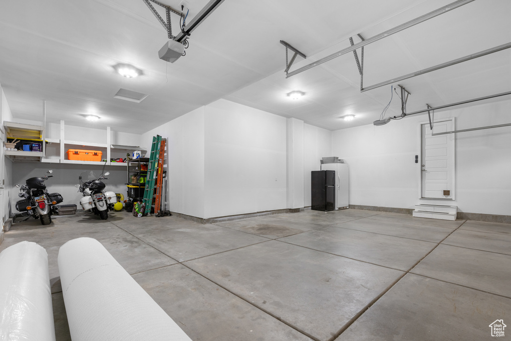 Garage featuring a garage door opener and freestanding refrigerator