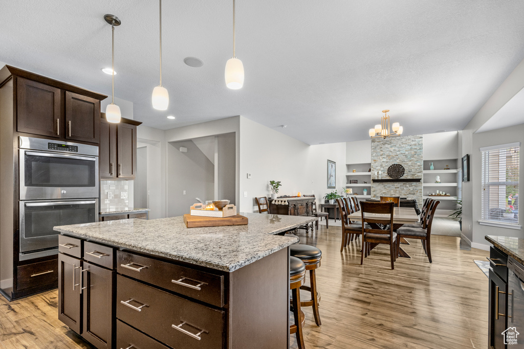 Kitchen featuring stainless steel double oven, light wood finished floors, a breakfast bar area, a center island, and dark brown cabinetry