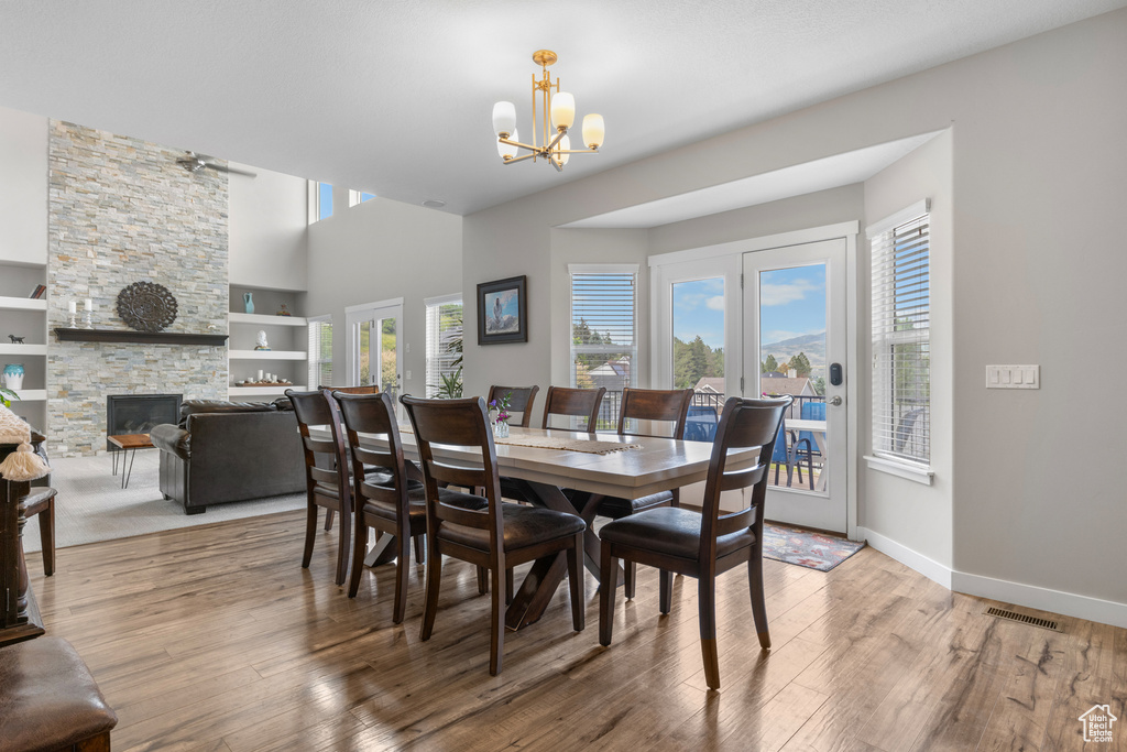 Dining space featuring a chandelier, wood finished floors, a fireplace, a high ceiling, and built in shelves