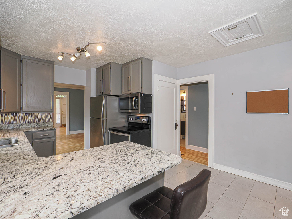 Kitchen featuring stainless steel appliances, a kitchen breakfast bar, a peninsula, light stone counters, and a textured ceiling