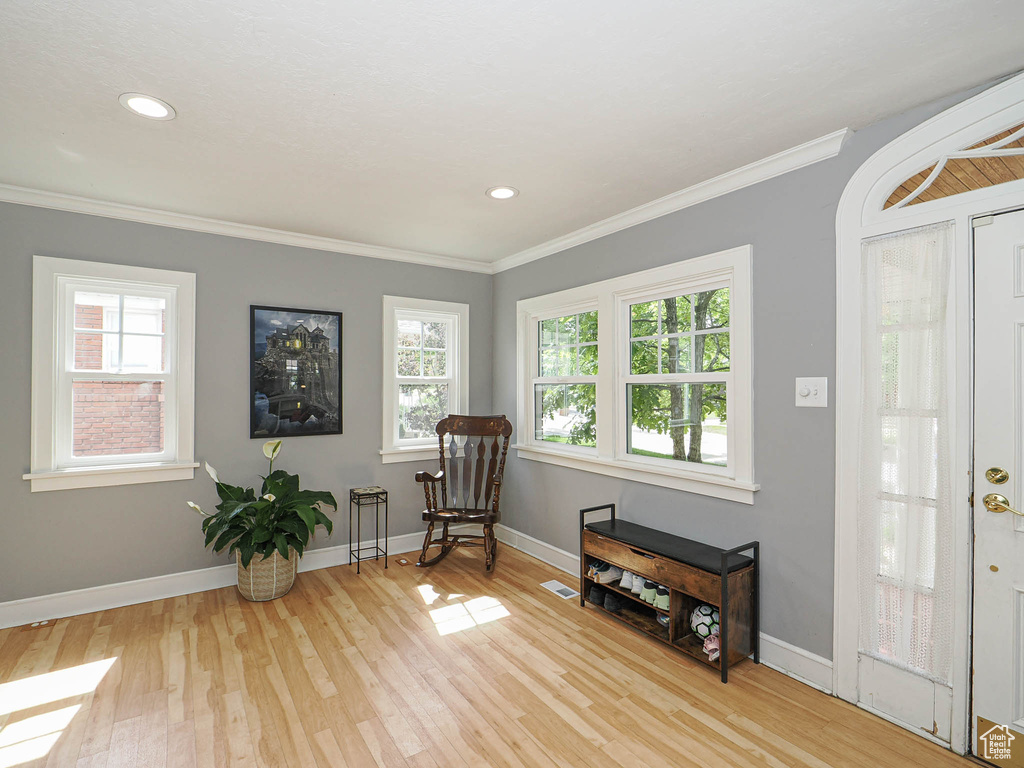 Living area with healthy amount of natural light, light wood finished floors, crown molding, and recessed lighting