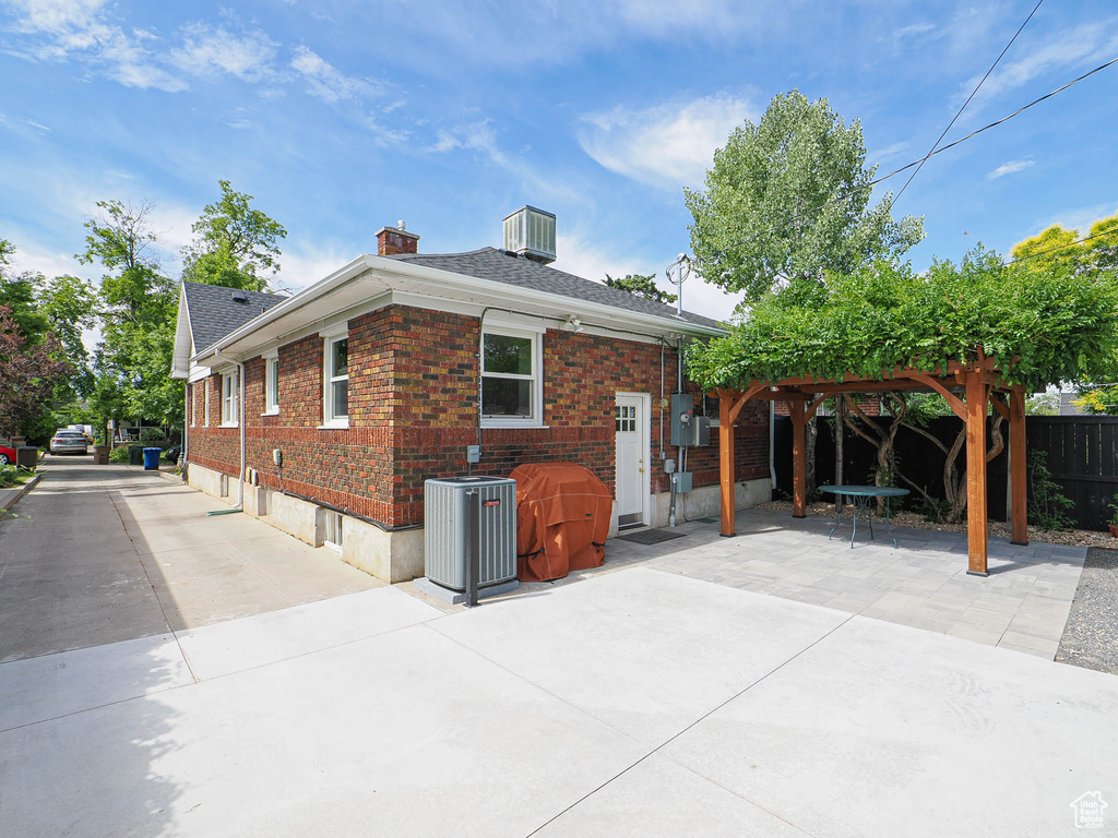 View of property exterior featuring a patio, brick siding, a chimney, and a shingled roof