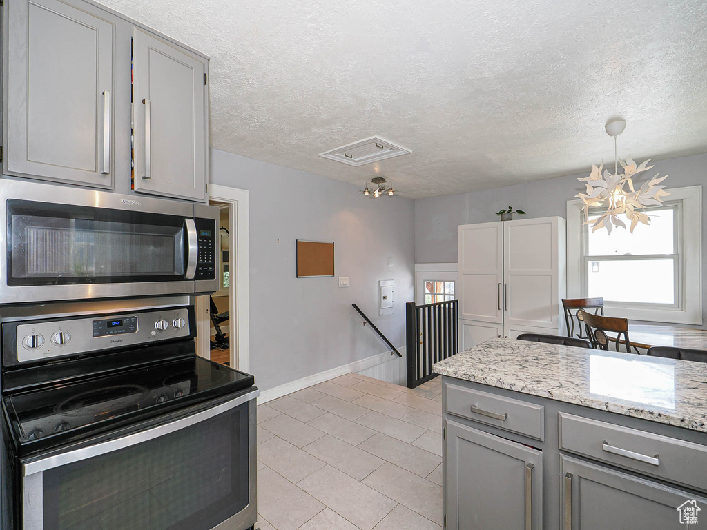 Kitchen with appliances with stainless steel finishes, gray cabinets, light tile patterned flooring, a textured ceiling, and light stone counters