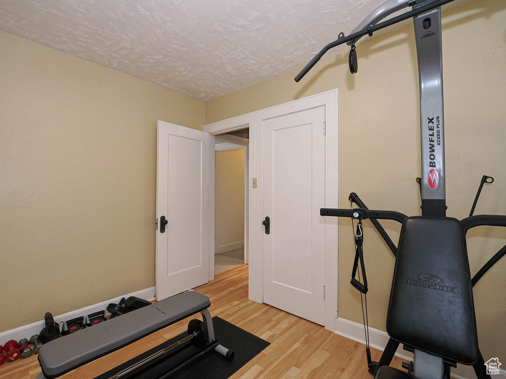 Exercise room with light wood-style floors and a textured ceiling
