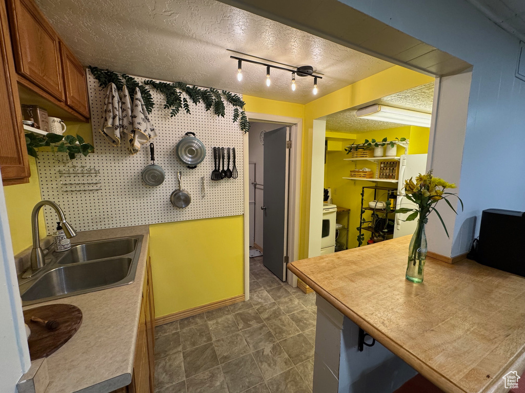 Kitchen with brown cabinets, a textured ceiling, freestanding refrigerator, and light countertops