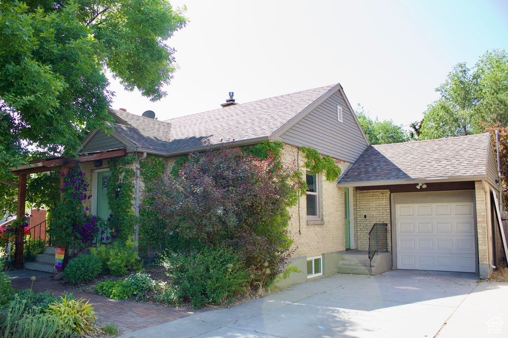 View of home's exterior featuring concrete driveway, roof with shingles, a garage, and brick siding