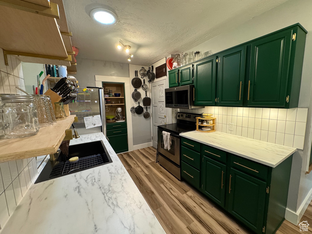 Kitchen with appliances with stainless steel finishes, green cabinetry, a textured ceiling, tasteful backsplash, and light wood-style floors
