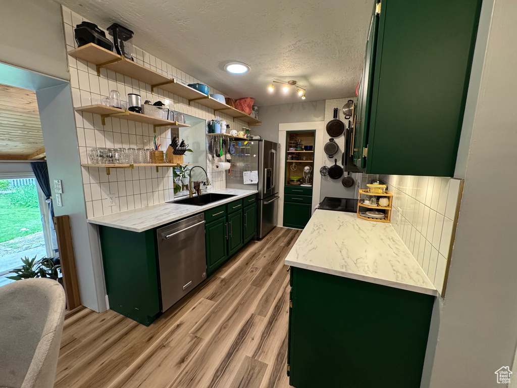 Kitchen with green cabinets, appliances with stainless steel finishes, decorative backsplash, light countertops, and a textured ceiling